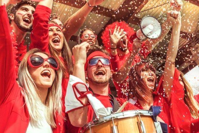 group of fans dressed in red color watching a sports event in the stands of a stadium using a black car service in the city.